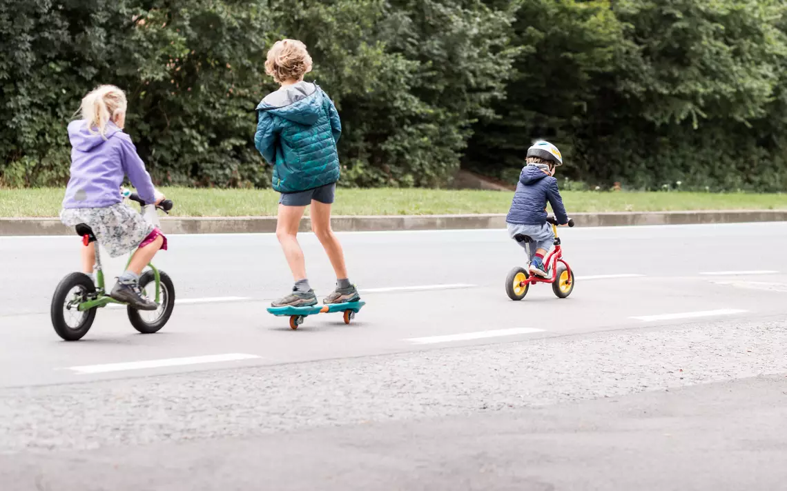 3 enfants en bas-âge sur un vélo, une draisienne et un skate